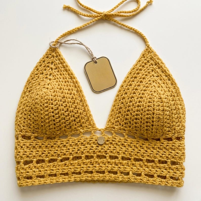 Puede incluir: Top halter de ganchillo amarillo mostaza con cuello en V profundo y bot&oacute;n decorativo. El top presenta una atadura halter y una etiqueta. El dise&ntilde;o de ganchillo incluye un patr&oacute;n calado decorativo en la parte inferior.