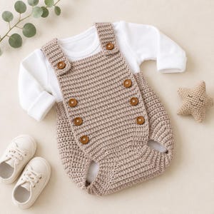Può includere: Una tutina all'uncinetto color beige con scollo quadrato e sei bottoni marroni, indossata sopra una maglietta bianca a maniche lunghe. Il set include un paio di scarpe da ginnastica bianche e un piccolo giocattolo a forma di stella all'uncinetto.