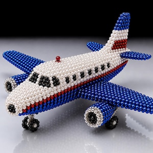 Pode incluir: Um modelo de avião decorativo construído com pequenas contas esféricas em branco, azul e vermelho. A fuselagem é principalmente branca com uma faixa vermelha, enquanto as asas e a cauda são azuis. Contas pretas formam as janelas da cabine.