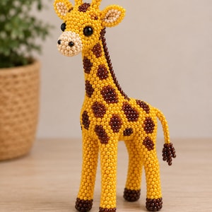 Op de afbeelding: Een staand giraffefiguurtje gemaakt van kleine gele, bruine en crèmekleurige kralen. De giraf heeft een lange nek, donkerbruine hoeven, twee kleine ossiconen op de kop en een staart met een pluizig uiteinde, alles opgebouwd uit kralenwerk.