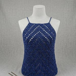 May include: A navy blue crochet halter top with a geometric design. The top is displayed on a mannequin and features a square neckline and thin straps. The crochet work has an open, airy pattern.