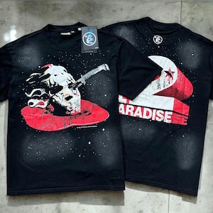 May include: A black short-sleeve t-shirt featuring a graphic of a skull with a knife and a red pool on the front, and a large red and white graphic with the text "2 PARADISE" on the back. The fabric has a subtle white speckled pattern.