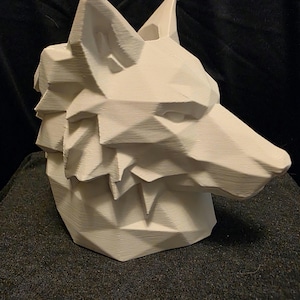 May include: A white, 3D-printed geometric wolf head sculpture featuring sharp, angular facets and a hollow top opening. The object displays a distinct layered texture characteristic of additive manufacturing, forming a stylized canine profile.