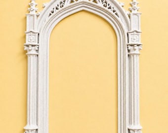 May include: A light gray, speckled, arched architectural frame featuring intricate vertical columns, a pointed top with decorative finials, and detailed carvings along the inner and outer edges, resembling a miniature gothic window structure.
