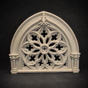 May include: A light beige, semi-circular architectural wall plaque featuring an intricate Gothic rose window design. The piece displays detailed stone-like tracery, including pointed arches, quatrefoil cutouts, and small columns on each side.