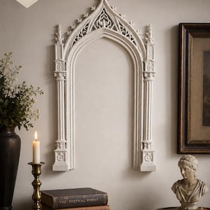 May include: A cream-colored wall-mounted arch featuring intricate architectural details, including pointed arches, columns, and finials. The piece measures 15 inches tall by 9 inches wide, displaying a textured surface with a stone-like appearance.