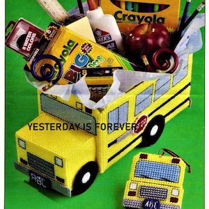 May include: A yellow school bus shaped plastic container filled with school supplies, including crayons, markers, pencils, an apple, and glue. The container has the text "YESTERDAY IS FOREVER" on the side. A smaller yellow school bus ornament is in the foreground.