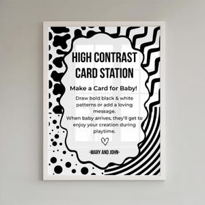 May include: A framed sign with the text "HIGH CONTRAST CARD STATION" in black. The sign encourages making a card for a baby with black and white patterns. The sign is decorated with black and white shapes and the names "MARY AND JOHN".