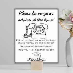 May include: A black and white framed sign featuring a rotary phone illustration and the text "Please leave your advice at the tone!". The sign encourages sharing memories. A wooden block supports the sign, with a vase of flowers.