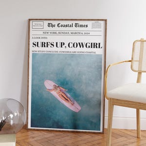 May include: A newspaper headline reads "Surfs Up, Cowgirl" with the subheading "New study conclude: Cowgirls are going coastal". The image shows a woman surfing on a pink surfboard in turquoise water.