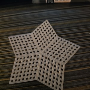 Op de afbeelding: Een witte plastic knutselrooster in de vorm van een ster. Het rooster is gemaakt van kleine, gelijkmatig verdeelde vierkanten, waardoor een open, roosterachtig ontwerp ontstaat. De ster heeft vijf punten, elk bestaande uit een deel van het rooster.