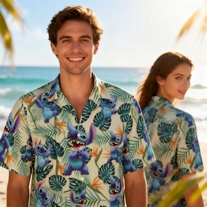 May include: Short-sleeved button-down shirt with a tropical pattern featuring the character Stitch from Lilo & Stitch. The shirt has a cream background with blue Stitch figures, green leaves, and orange flowers. The shirt is worn by two people on a beach.