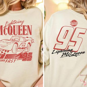 K&ouml;nnte beinhalten: Ein hellbeiger Pullover mit einem roten Aufdruck eines Cartoon-Rennwagens mit dem Text "Lightning McQueen" und "Think Fast" auf der Vorderseite. Die R&uuml;ckseite des Pullovers hat eine gro&szlig;e rote Nummer "95" mit dem Text "Lightning McQueen" darunter.