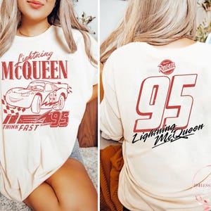 K&ouml;nnte beinhalten: Ein wei&szlig;es T-Shirt mit einer roten Grafik von Lightning McQueen aus dem Disney Pixar Film Cars. Die Grafik enth&auml;lt den Text "Lightning McQueen", "Think Fast" und "95". Die R&uuml;ckseite des Shirts hat eine rote Grafik der Nummer "95" mit dem Text "Lightning McQueen" und dem Rust-eze Logo.