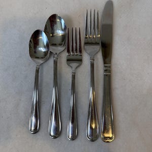 May include: A set of stainless steel silverware including two spoons, two forks, and a knife. The silverware has a simple, elegant design with rounded handles and a polished finish. The spoons are different sizes.
