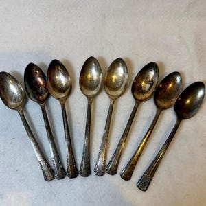 May include: An assortment of eight vintage silver spoons. The spoons have oval bowls and long, slender handles. Some handles have a decorative pattern. The spoons show signs of age and use, with some tarnishing and wear on the silver.