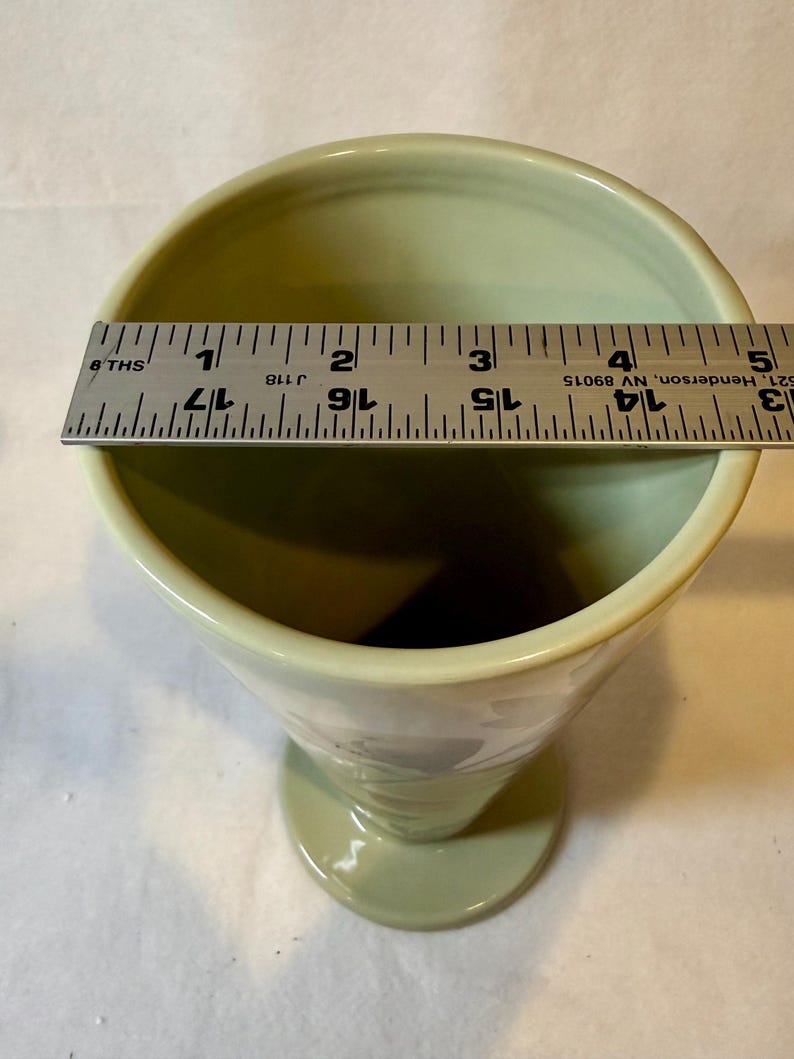 Puede incluir: Un c&aacute;liz de cer&aacute;mica verde p&aacute;lido con la parte superior ensanchada y una base de pedestal. El borde mide aproximadamente 7,6 cm de di&aacute;metro. Se coloca una regla sobre la parte superior del c&aacute;liz para medir.