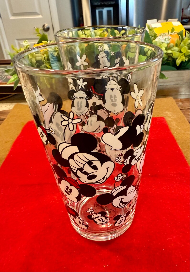 Puede incluir: Vasos de vidrio transparente con un patr&oacute;n repetido de personajes de Mickey y Minnie Mouse en negro, blanco y rojo. Los vasos son cil&iacute;ndricos y adecuados para bebidas. El dise&ntilde;o incluye acentos florales.