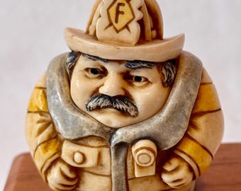 This is a "Flame Tamer" firefighter figurine from the Harmony Kingdom / Harmony Ball Company Pot Bellys collection.