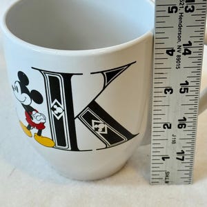 May include: A white ceramic mug with a black handle and the text "But First, Coffee" in a bold, black font. The mug is set against a blurred background, suggesting a cosy setting.