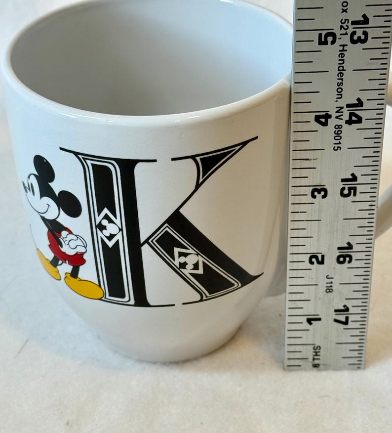 May include: A white ceramic mug with a black handle and the text "But First, Coffee" in a bold, black font. The mug is set against a blurred background, suggesting a cosy setting.