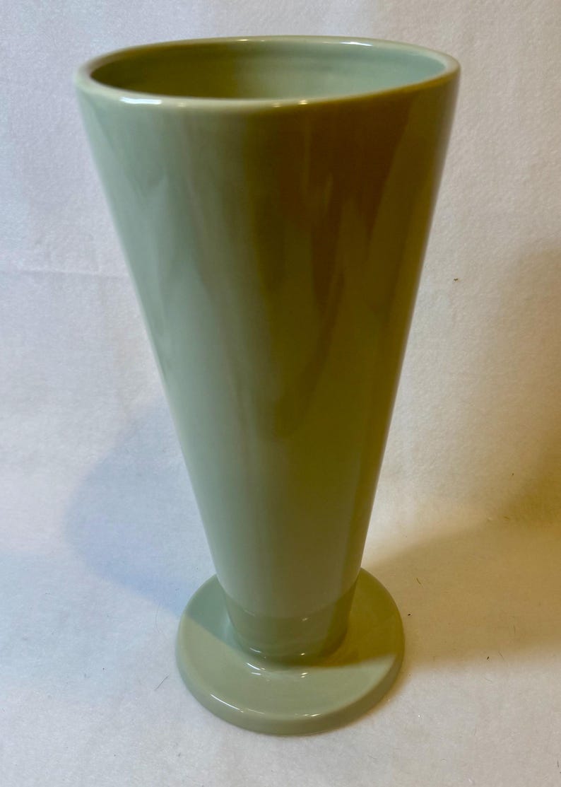 Puede incluir: Una taza de cer&aacute;mica blanca con un asa negra y el texto "But First, Coffee" en un estilo manuscrito. La taza est&aacute; sobre una superficie blanca. La taza mide aproximadamente 10 cm de alto.