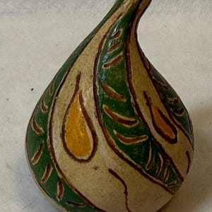 May include: A pear-shaped gourd with a smooth, light beige base color. The surface features hand-painted green leaf patterns with dark brown outlines and small, solid yellow teardrop-shaped accents distributed across the exterior.