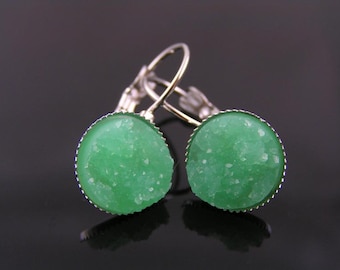 May include: A pair of round, lever-back earrings. Each earring features a vibrant green, textured stone set in a silver-colored, scalloped bezel. The earrings are displayed against a dark background.