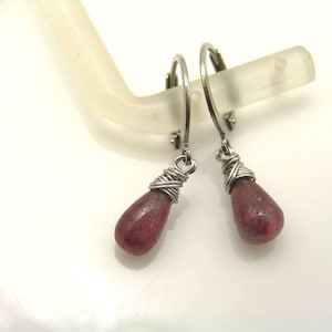 May include: A pair of silver hoop earrings with a teardrop-shaped pink stone dangling from each hoop. The stones are wrapped in silver wire.