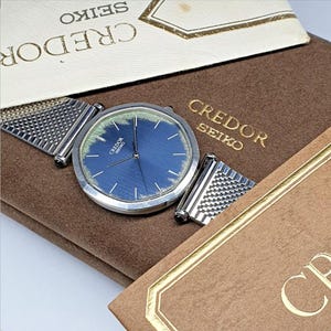 May include: A silver watch with a blue face and a silver mesh band. The watch is in a brown box with the word "CREDOR SEIKO" printed on it.