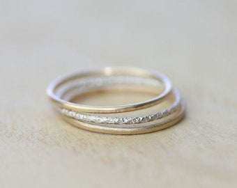 May include: A set of three thin gold and silver rings stacked on top of each other. The silver ring has a textured surface.