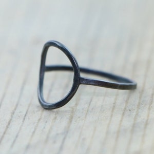 Può includere: Un anello d'argento semplice e minimalista con un design circolare aperto e arrotondato. L'anello è ossidato, il che gli conferisce una finitura scura e antica.