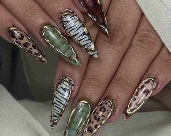 May include: A hand with long, pointed fingernails. The nails feature various designs, including animal prints like leopard spots and zebra stripes, and solid colors. Each nail is outlined with a gold-colored trim.