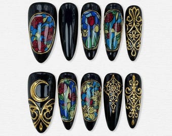 May include: A set of ten black, almond-shaped press-on nails. Designs include stained glass patterns with red roses and blue accents, gold filigree, a gold crescent moon, and a gold spiderweb. The nails are arranged on a white surface.