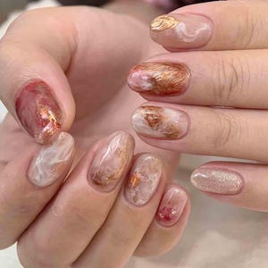 Könnte beinhalten: Nahaufnahme einer Hand mit mehreren manikürten Nägeln. Die Nägel weisen eine Vielzahl von Designs auf, darunter Marmoreffekte, Goldfolienakzente und Glitzer. Farben sind Rosa-, Rot-, Gold- und Weißtöne, die einen stilvollen und künstlerischen Look erzeugen.