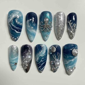 May include: A collection of ten almond-shaped artificial nails with ocean-themed designs. The nails feature shades of blue, white, and silver, with wave patterns, glitter, and seashell or octopus embellishments. Some nails have pearl accents.