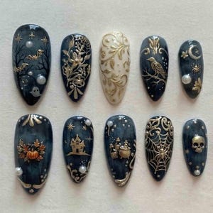 May include: A set of ten press-on nails featuring dark blue and cream backgrounds with gold metallic accents. Designs include bats, a haunted house, a skull, a spider web, a raven, a pumpkin, potion bottles, and small white pearl embellishments.