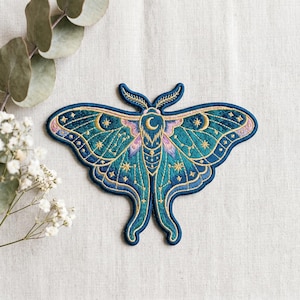 May include: Embroidered moth patch in shades of teal, blue, and gold. The patch features a detailed design with celestial elements like stars and a crescent moon. The moth's wings are spread, showcasing intricate stitching and a delicate, colorful pattern.