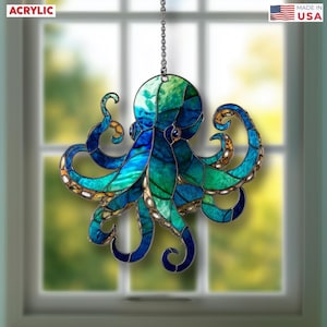 May include: A stained glass-style octopus ornament in shades of blue and green, hanging from a chain. The word "ACRYLIC" is in the upper left corner. The ornament is suspended in front of a window.
