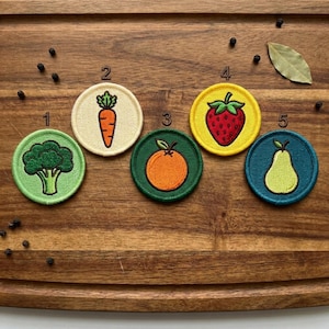 May include: Five circular embroidered patches featuring food illustrations labeled with numbers one through five. The patches depict a green broccoli, an orange carrot, an orange fruit, a red strawberry, and a light green pear on various colored backgrounds.