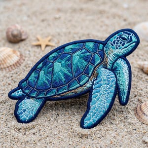 May include: Embroidered sea turtle patch in shades of blue and teal, with intricate stitching details. The patch is set against a sandy background with seashells and a starfish, evoking a beach theme. The turtle's design features a detailed shell and flippers.