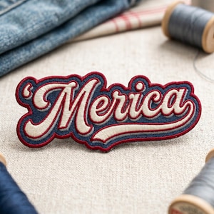 May include: Embroidered patch with the word "Merica" in a retro script. The patch features a navy blue background with white and red accents, and a red border. The patch is likely for clothing or accessories.