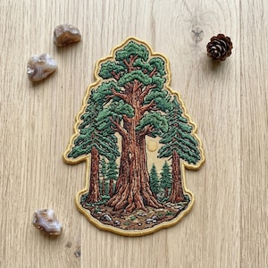 May include: An embroidered patch featuring a large central redwood tree with thick brown bark and green foliage, flanked by two smaller trees. The background is a light tan color with a small yellow sun, all enclosed in a gold-stitched border.