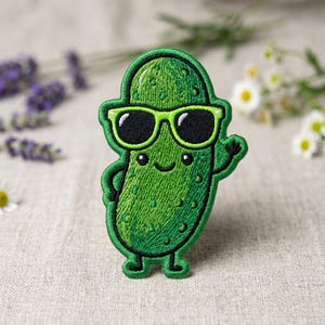 May include: Embroidered patch featuring a smiling green pickle wearing sunglasses. The patch has a green border and is waving with one hand. The pickle has a textured surface and is a fun, whimsical design.