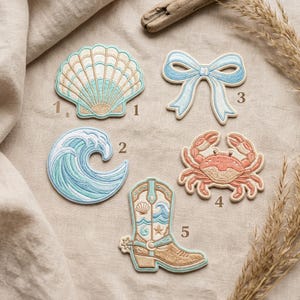 May include: A collection of embroidered patches with a coastal theme. Designs include a seashell, a wave, a bow, a crab, and a cowboy boot. The patches feature light blue, tan, and coral colors.