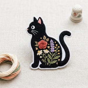May include: An embroidered patch shaped like a sitting black cat with a white outline. The cat's body features a colorful floral design including a large coral rose, purple lavender sprigs, white daisies, and small yellow buds with green leaves.