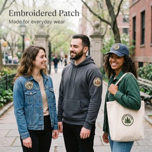 May include: Three people wearing outdoor-themed apparel. A woman wears a denim jacket with an embroidered patch. A man wears a gray hoodie with a similar patch. Another woman holds a tote bag and wears a cap, both with nature-themed designs. The text "Embroidered Patch Made for everyday wear" is at the top.