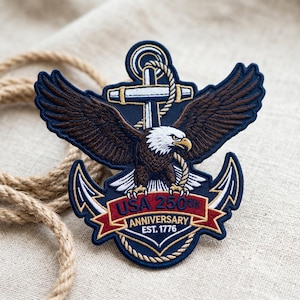 May include: Embroidered patch featuring a bald eagle with outstretched wings, perched atop an anchor. The patch is navy blue, brown, white, and red, with the text "USA 250th Anniversary EST. 1776". A rope is visible in the background.