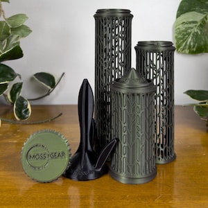 May include: A set of dark green and black 3D printed components including two tall cylindrical lattice structures, a shorter cylindrical piece with a pointed top, a black tripod-like stand, and a round olive green cap with the text MOSSYGEAR.