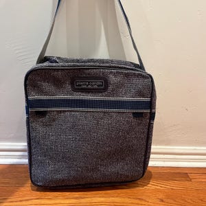 May include: A gray and blue Pierre Cardin shoulder bag with a zipper closure and a black strap. The bag has a white and blue striped design.